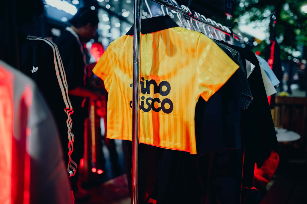 Yellow sports jersey with 'Vino Disco' branding on a rack in a store.