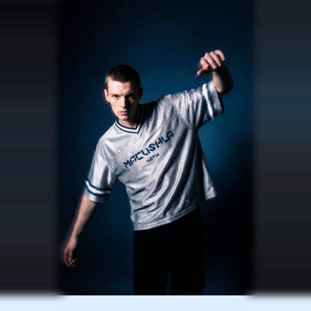 Editorial shot of the gray boxy striped soccer jersey by Merch in Town x Guillaume Michaud, arm raised under studio haze.