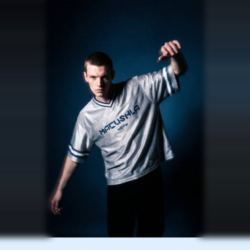 Editorial shot of the gray boxy striped soccer jersey by Merch in Town x Guillaume Michaud, arm raised under studio haze.
