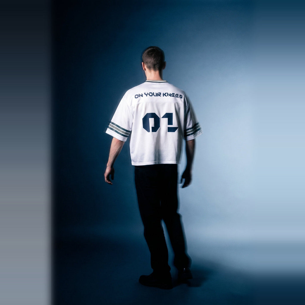 Back view of the white boxy striped soccer jersey by Merch in Town x Guillaume Michaud, showing the ON YOUR KNEES 01 print.