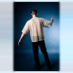 Back view of the beige mesh tee by Merch in Town x Guillaume Michaud, worn with black trousers.