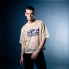 Portrait of the beige mesh NSFW tee by Merch in Town x Guillaume Michaud, worn with black trousers.