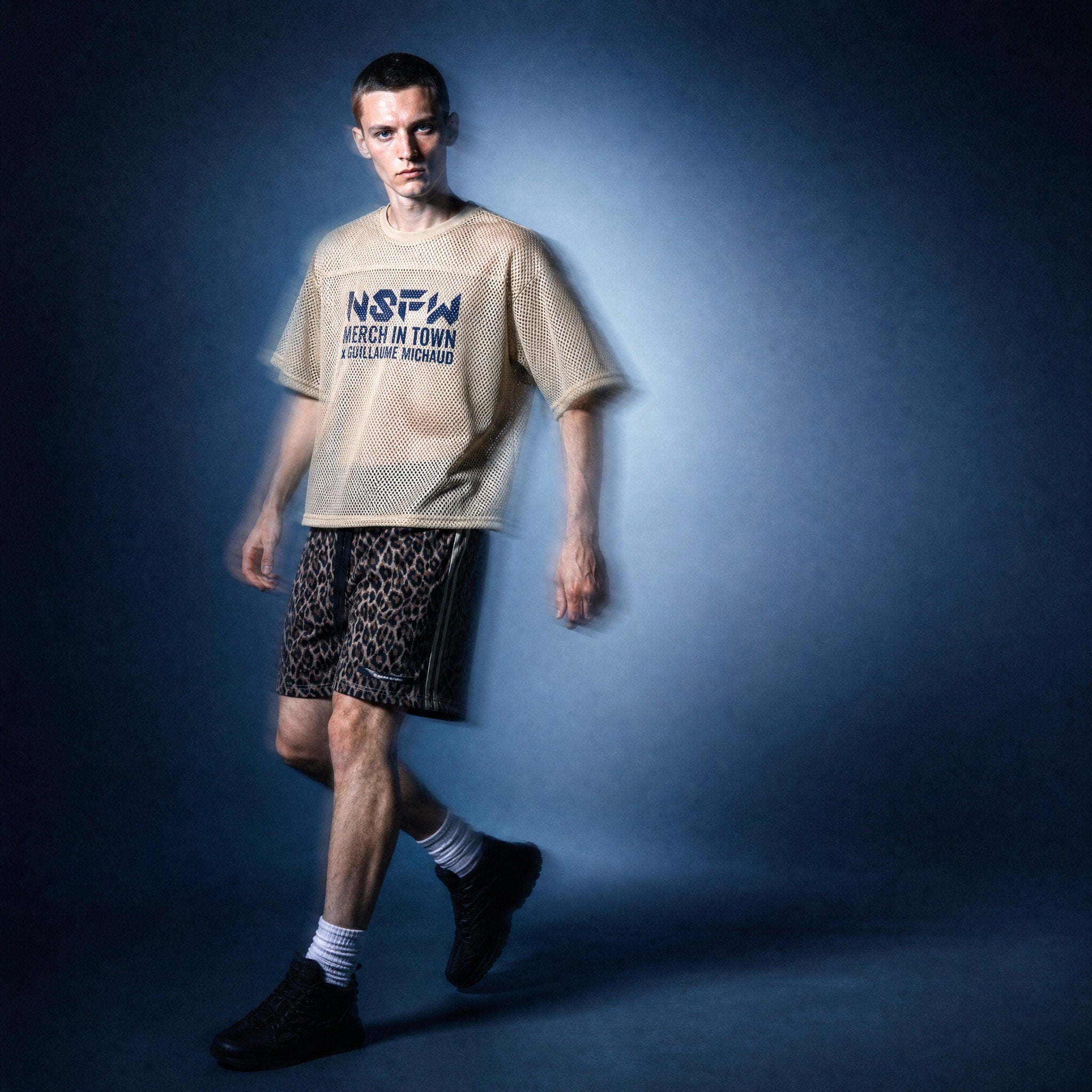 Model in beige mesh NSFW tee by Merch in Town x Guillaume Michaud, styled with leopard drawstring shorts and black sneakers.