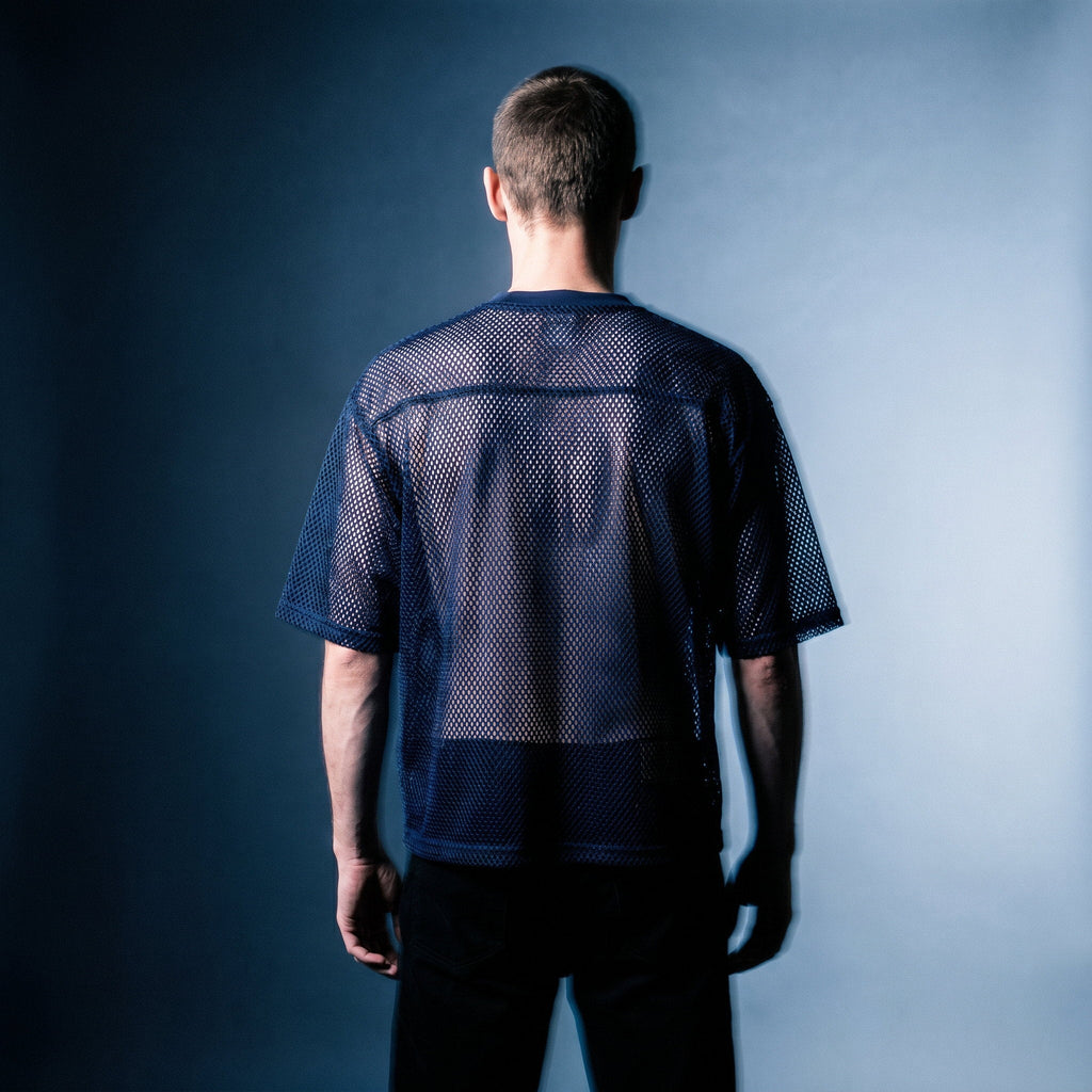 Back view of the navy mesh tee by Merch in Town x Guillaume Michaud, worn with black trousers.