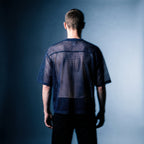 Back view of the navy mesh tee by Merch in Town x Guillaume Michaud, worn with black trousers.