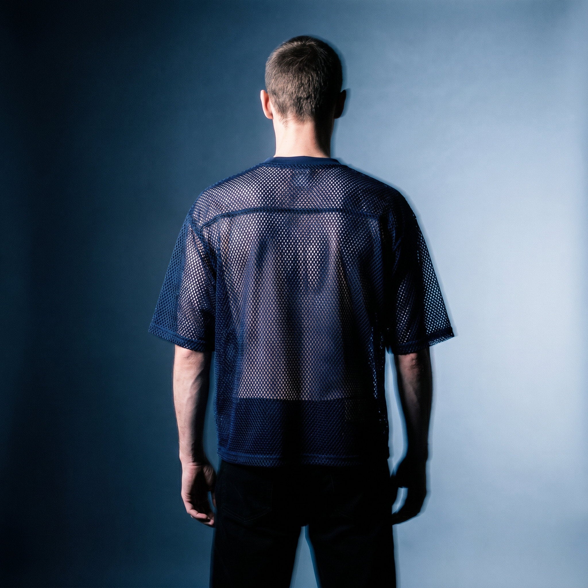 Back view of the navy mesh tee by Merch in Town x Guillaume Michaud, worn with black trousers.