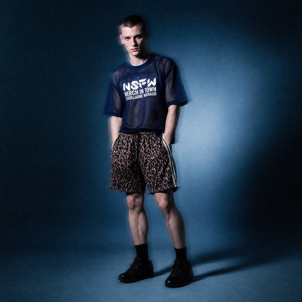 Full-length shot of the navy mesh NSFW tee by Merch in Town x Guillaume Michaud with leopard drawstring shorts and black sneakers.