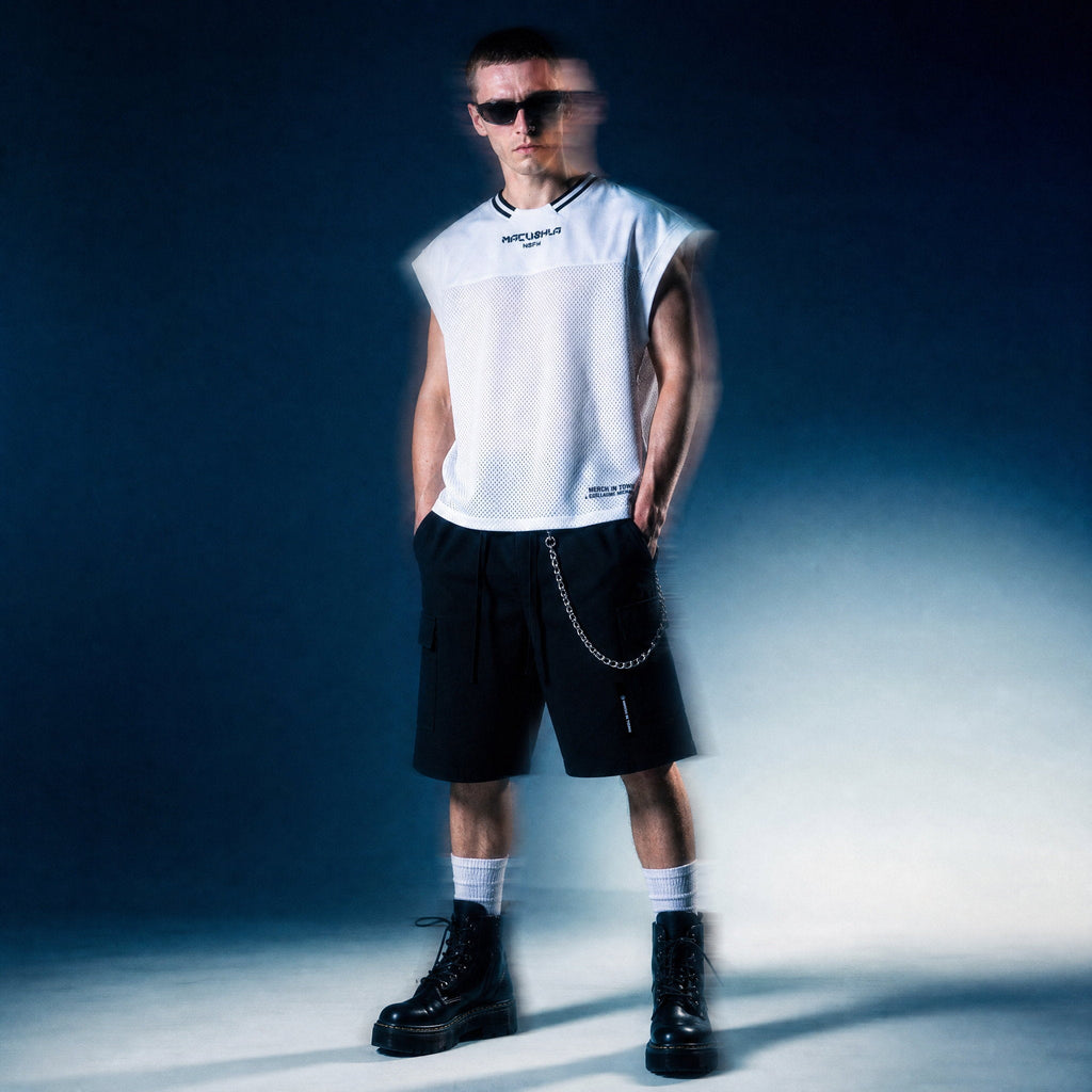 Model in white sleeveless mesh MACUSHLA tee by Merch in Town x Guillaume Michaud, worn with black drawstring cargo shorts and platform boots.