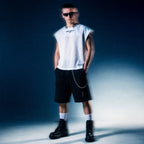 Model in white sleeveless mesh MACUSHLA tee by Merch in Town x Guillaume Michaud, worn with black drawstring cargo shorts and platform boots.