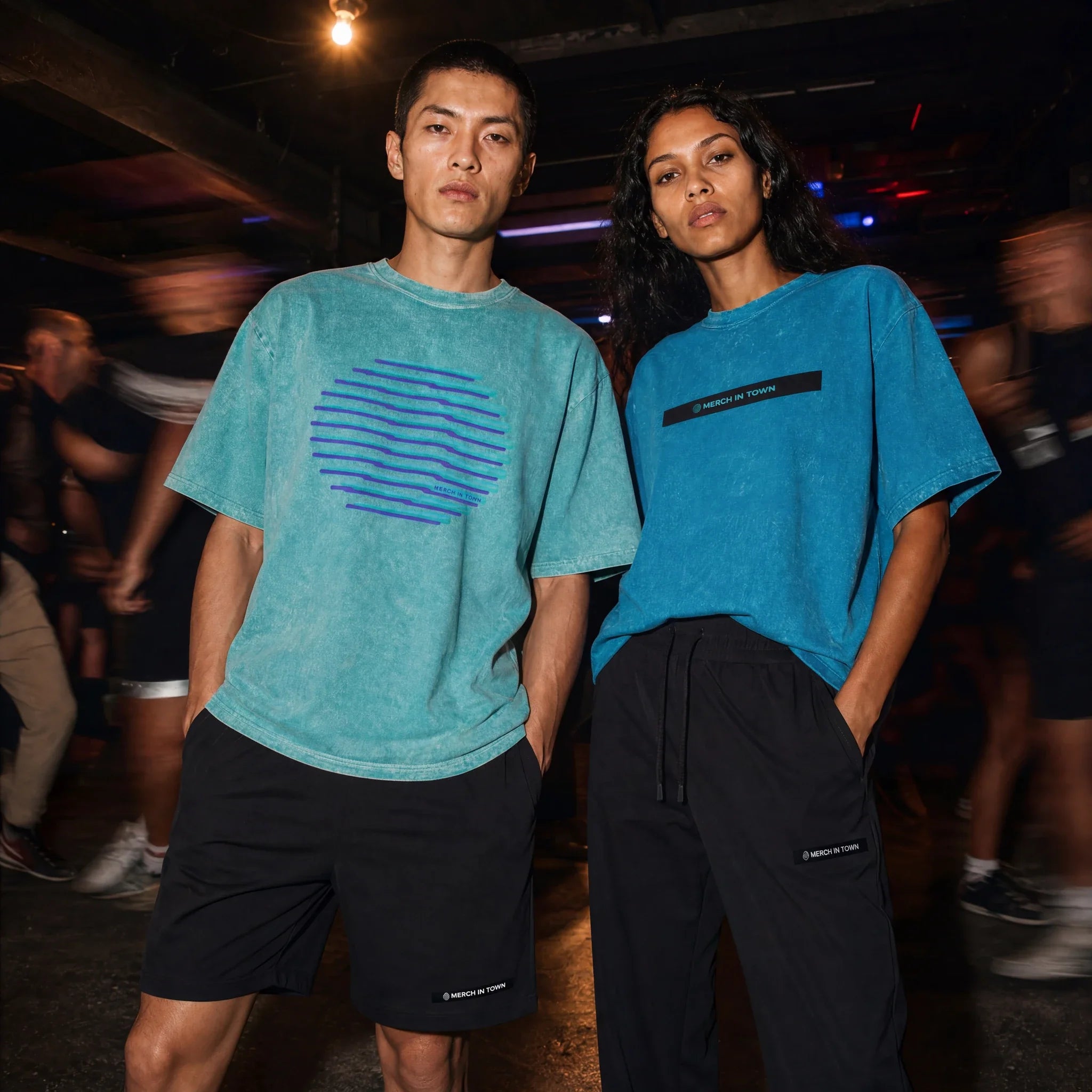 Two models in Merch in Town snow washed tees and black bottoms at an underground club.