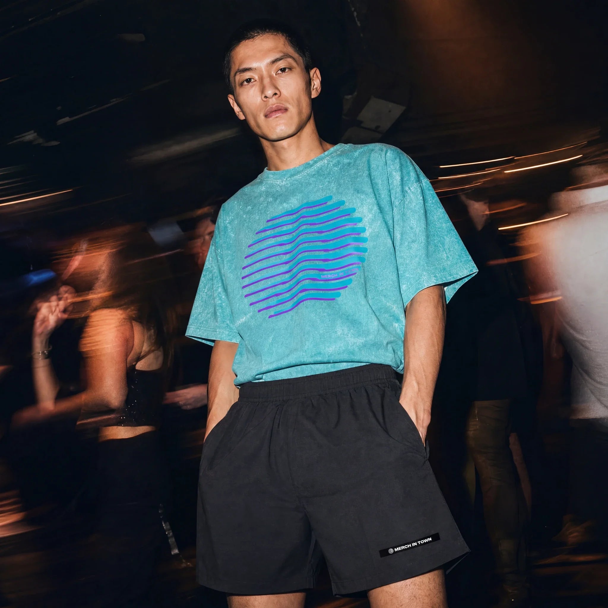 Model in a Merch in Town snow washed tee and black elastic waist shorts at an underground club.
