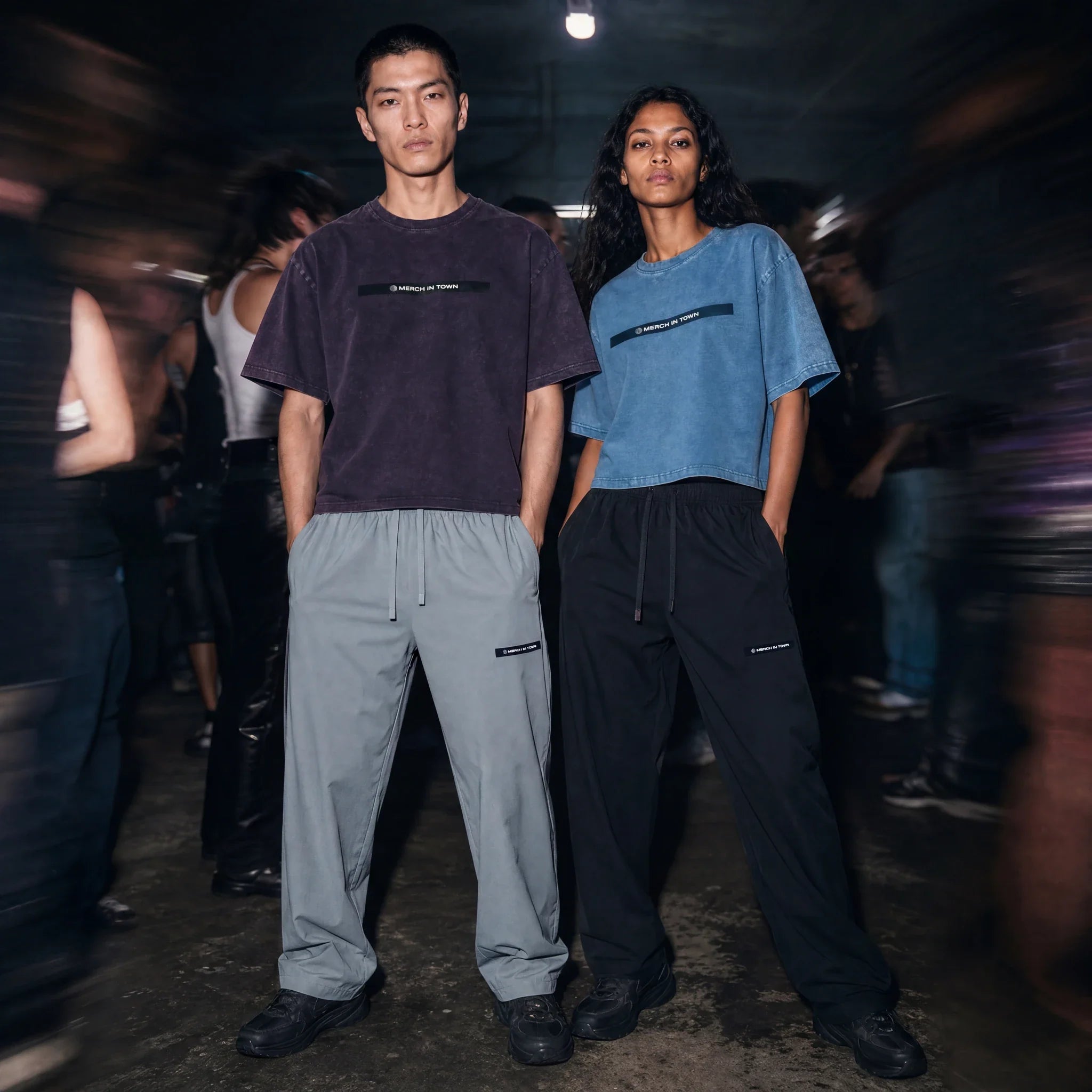 Two models in Merch in Town tees and Lightweight Tapered Track Pants at an underground club.