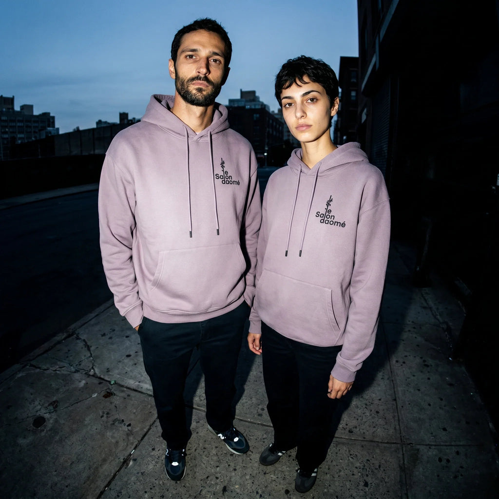 Two people wearing the Salon Daomé ash purple fleece hoodie on a city sidewalk at dusk.