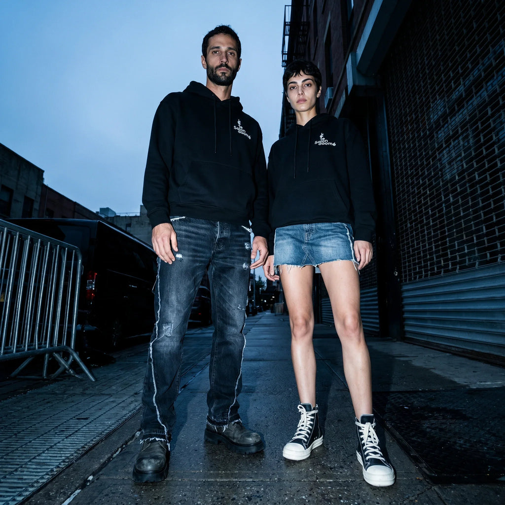 Two people wearing the Salon Daomé black fleece hoodie on an evening city street.