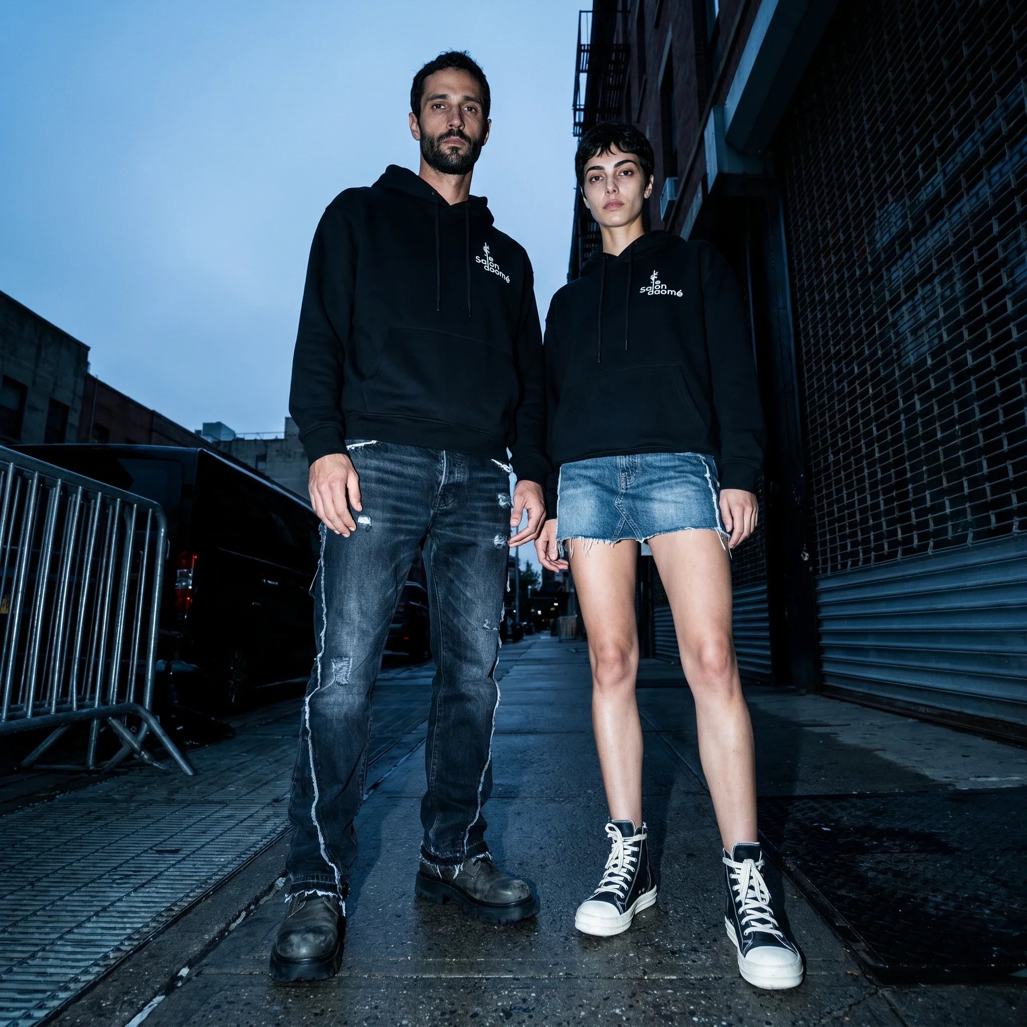 Two people wearing the Salon Daomé black fleece hoodie on an evening city street.