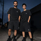 Two people wearing the Salon Daomé black mineral wash raw edge t-shirt and shorts set at dusk.