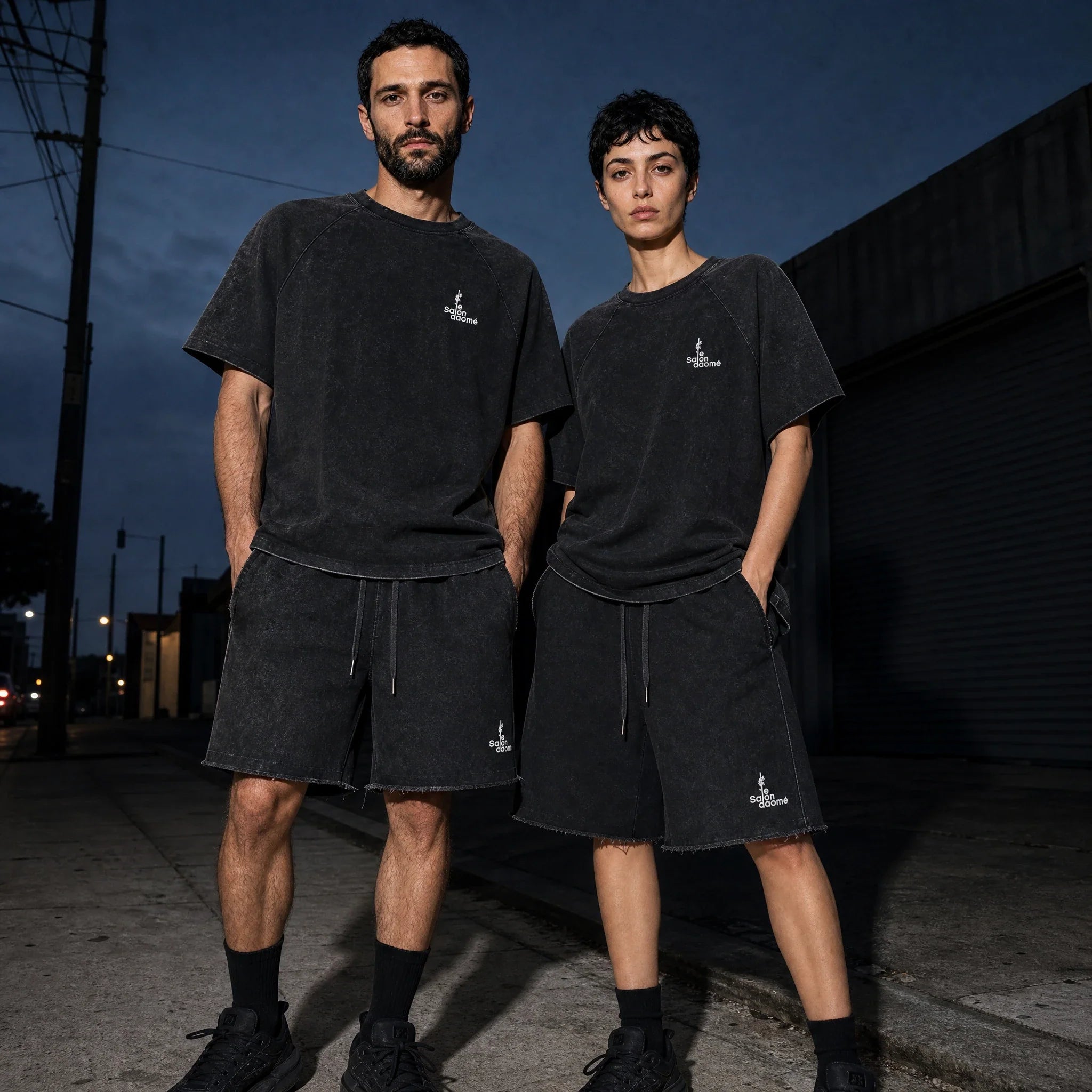Two people wearing the Salon Daomé black mineral wash raw edge t-shirt and shorts set at dusk.