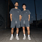 Two people wearing the Salon Daomé mineral wash raw edge t-shirt and shorts set in medium gray on a city street.