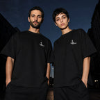 Two people wearing the Salon Daomé black Sorona quick-dry boxy t-shirt on an evening street.