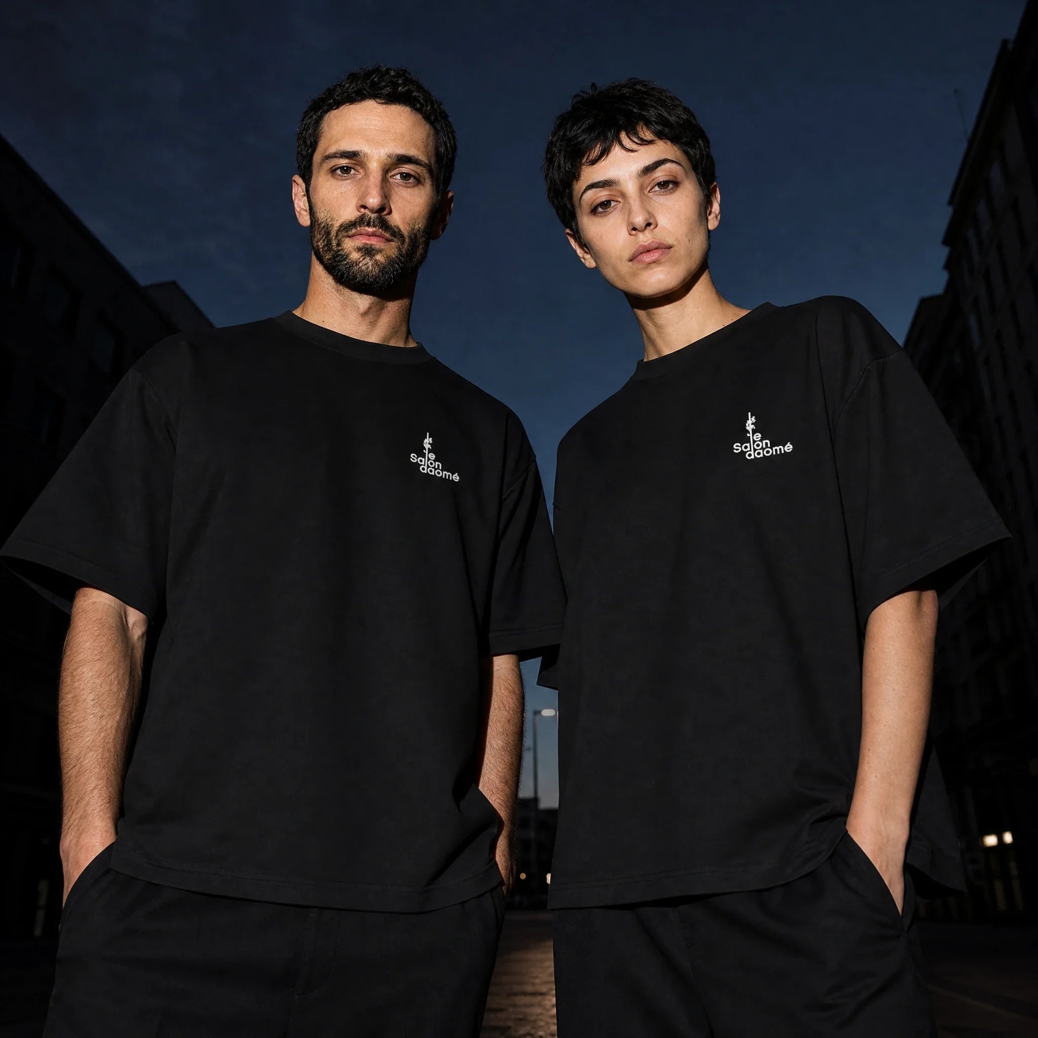 Two people wearing the Salon Daomé black Sorona quick-dry boxy t-shirt on an evening street.
