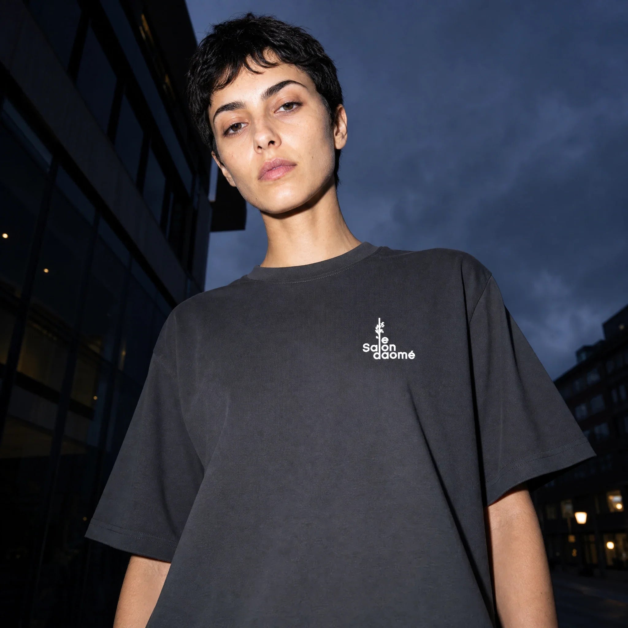 Salon Daomé dark grey Sorona quick-dry boxy t-shirt, oversized fit, on a city street at dusk.
